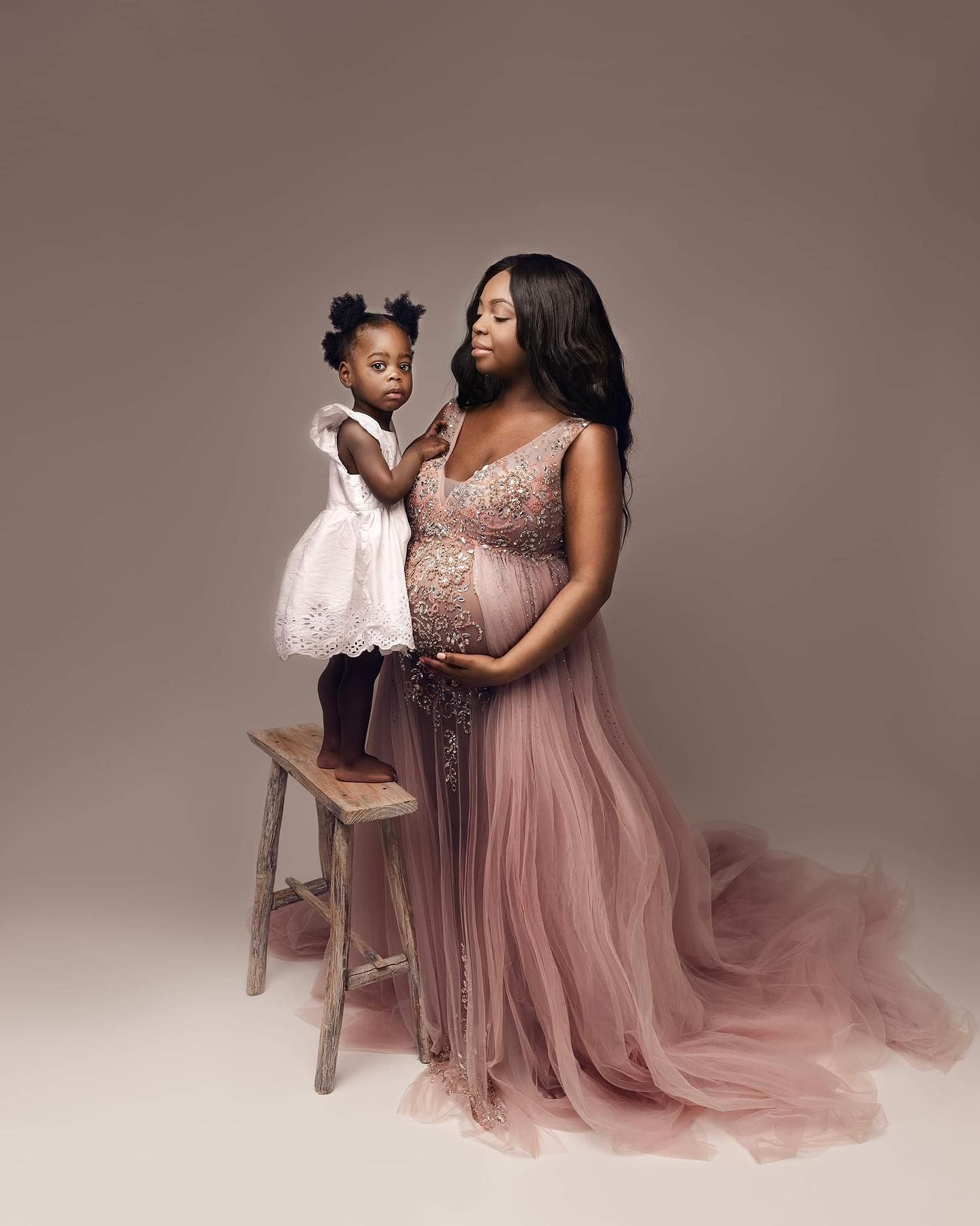 A mother and child in matching pink outfits pose together for a series of elegant studio portraits.