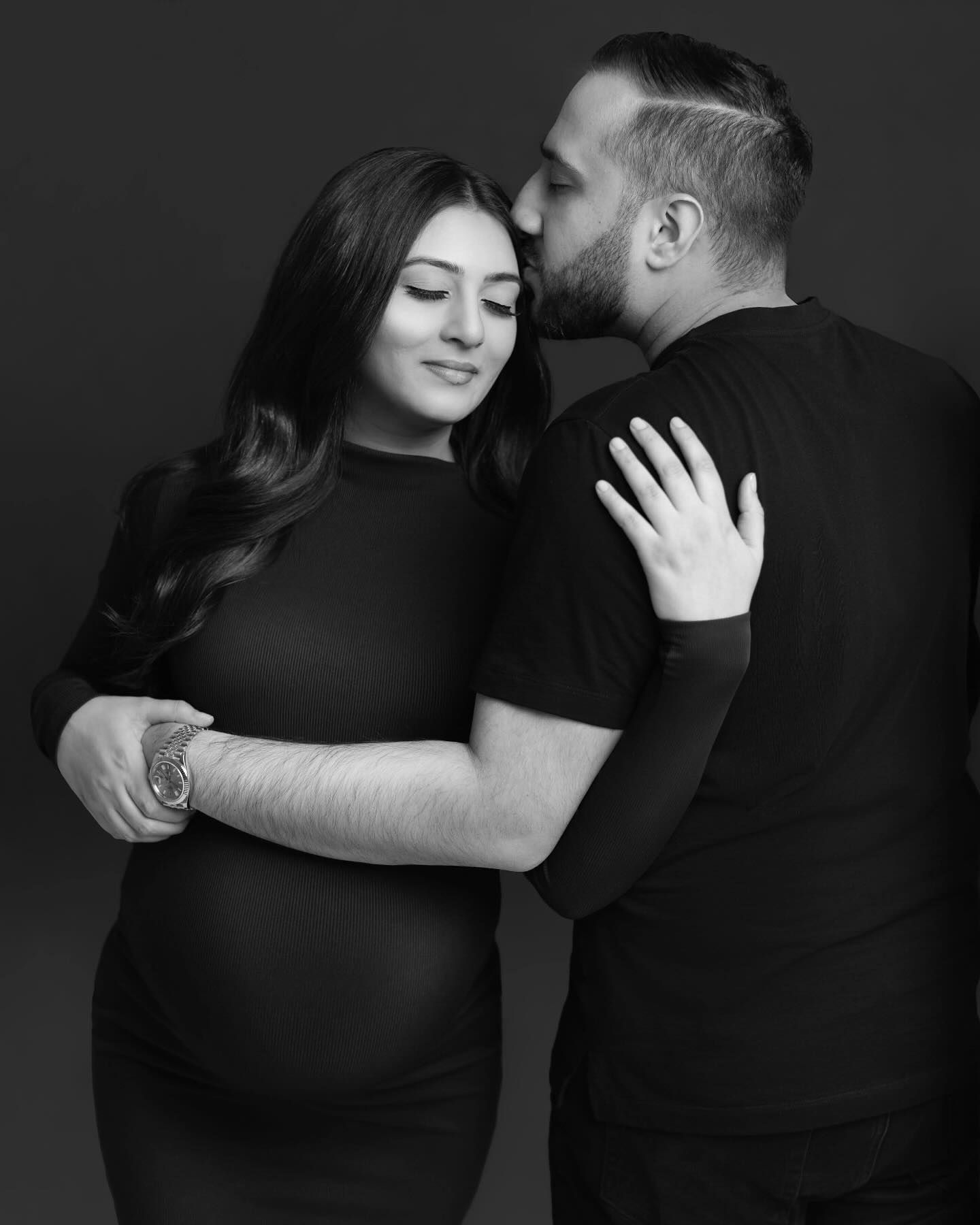 A series of black and white intimate portraits showing a couple embracing in romantic poses against a dark background.
