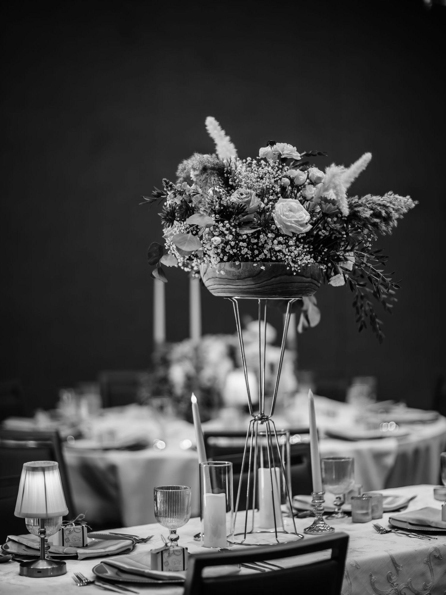An elegant black and white wedding centerpiece with tall glass vase and floral arrangement on a formal dining table.