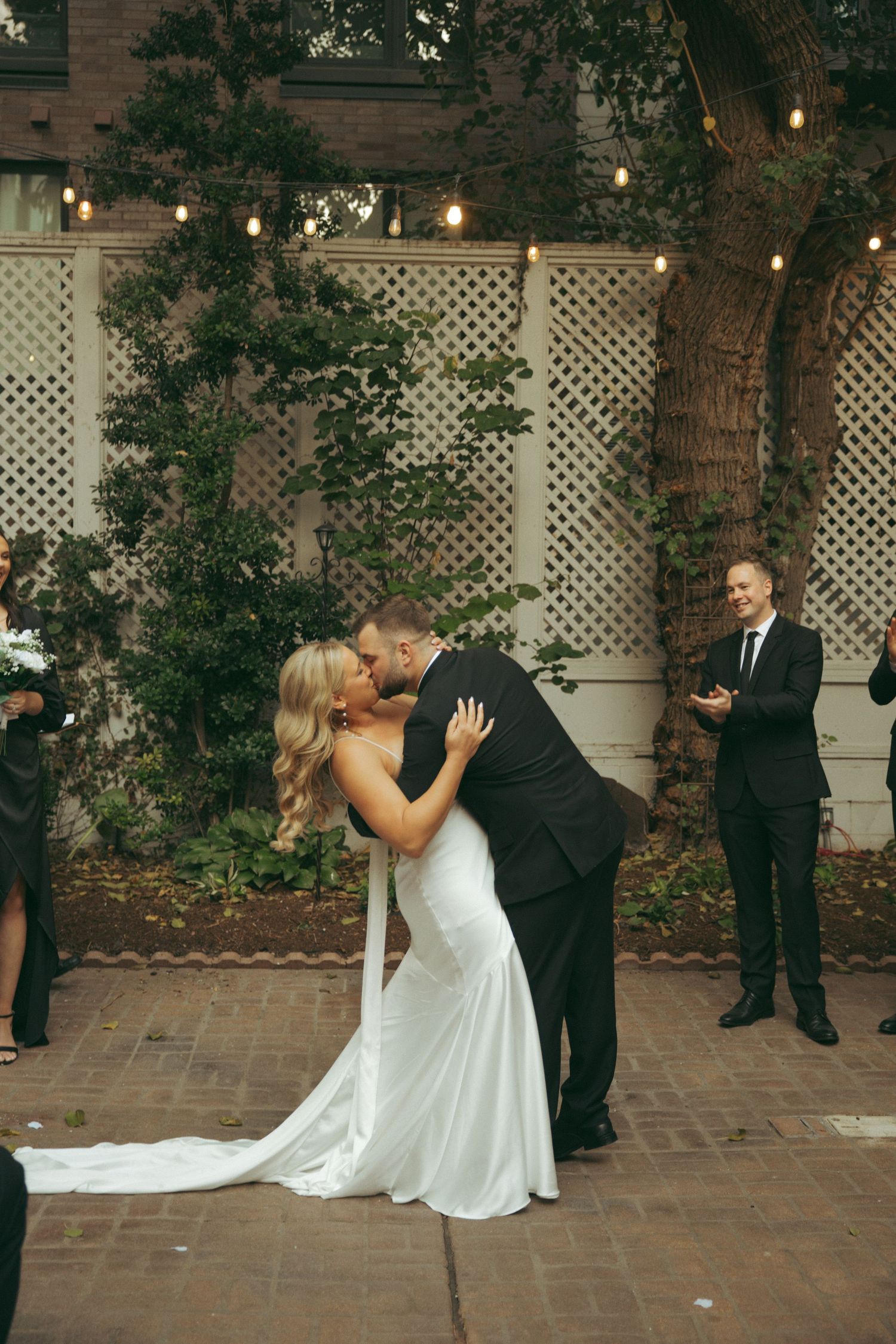 A romantic wedding couple dances and dips in sequence under string lights on an outdoor patio with lattice decor.