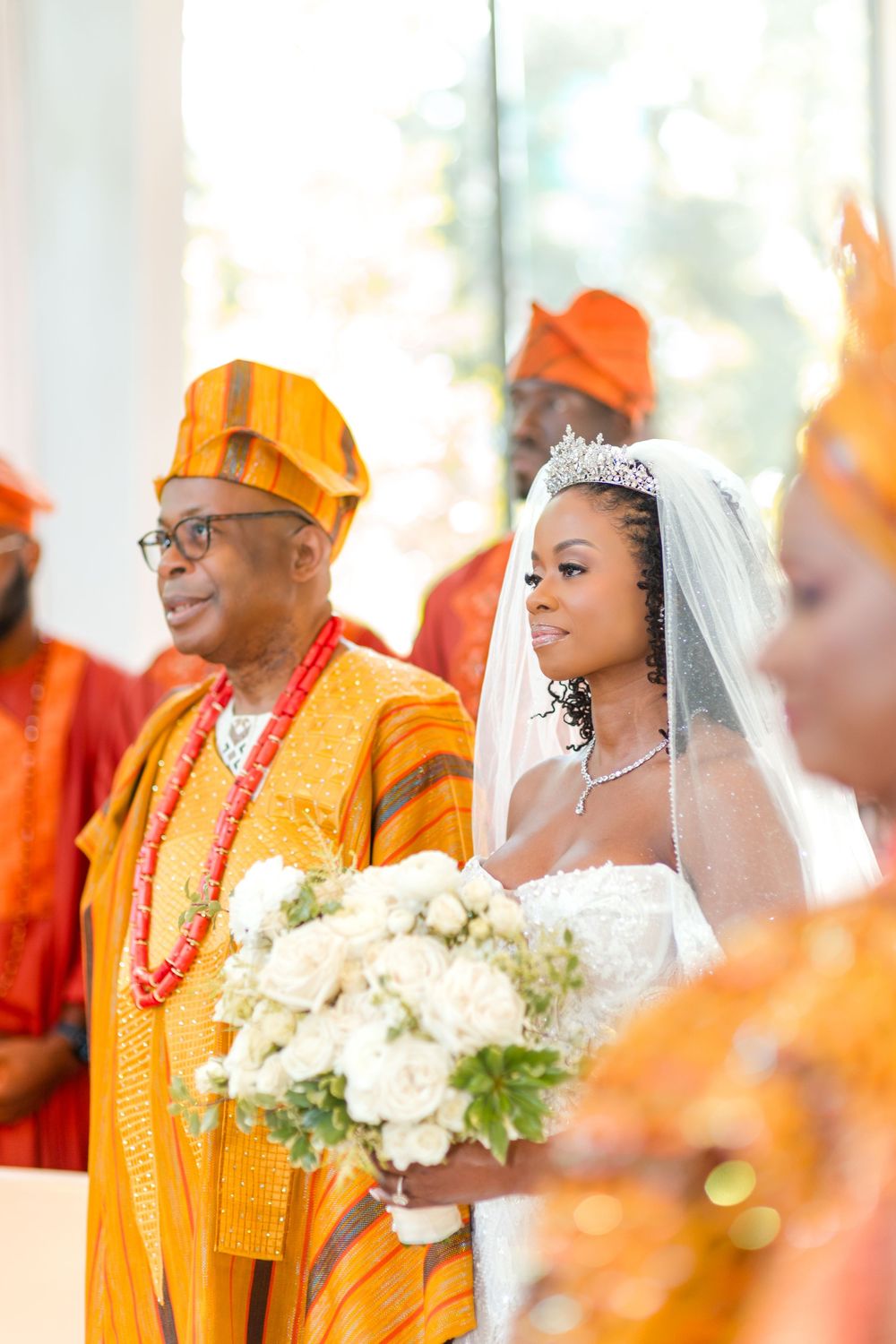 A traditional wedding ceremony with attendees wearing vibrant orange attire and cultural beaded necklaces.