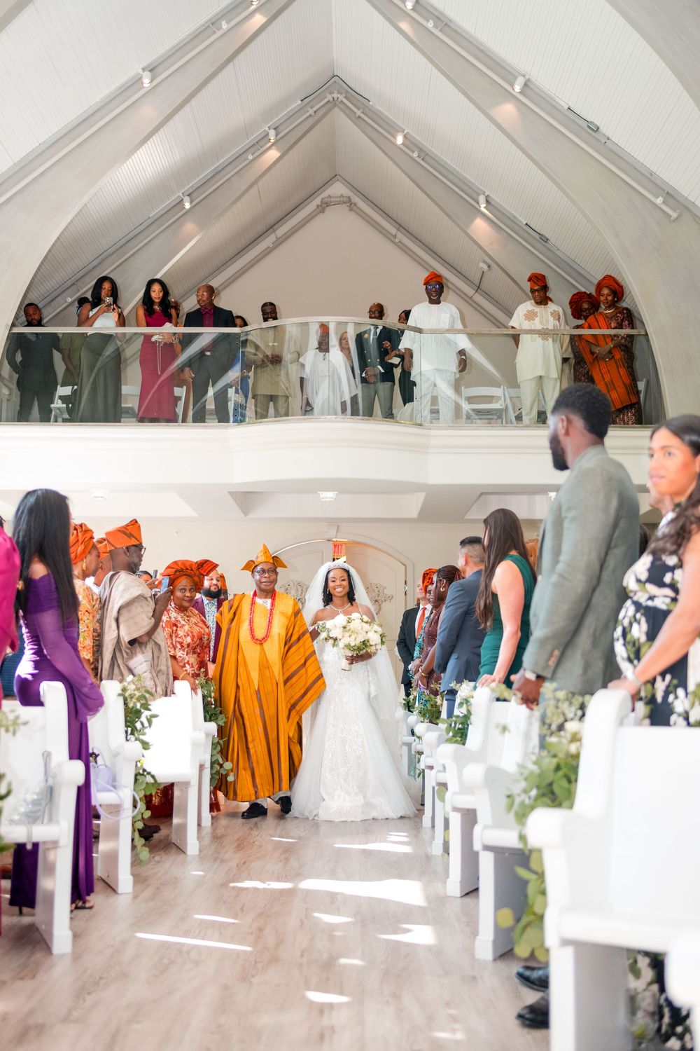 Wedding guests in traditional African attire gather inside a bright white tent during a multicultural celebration.