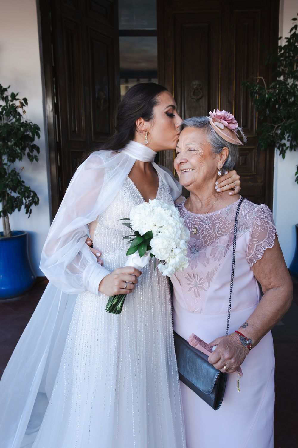 A bride in a white dress shares tender moments with an older woman in a lace dress.
