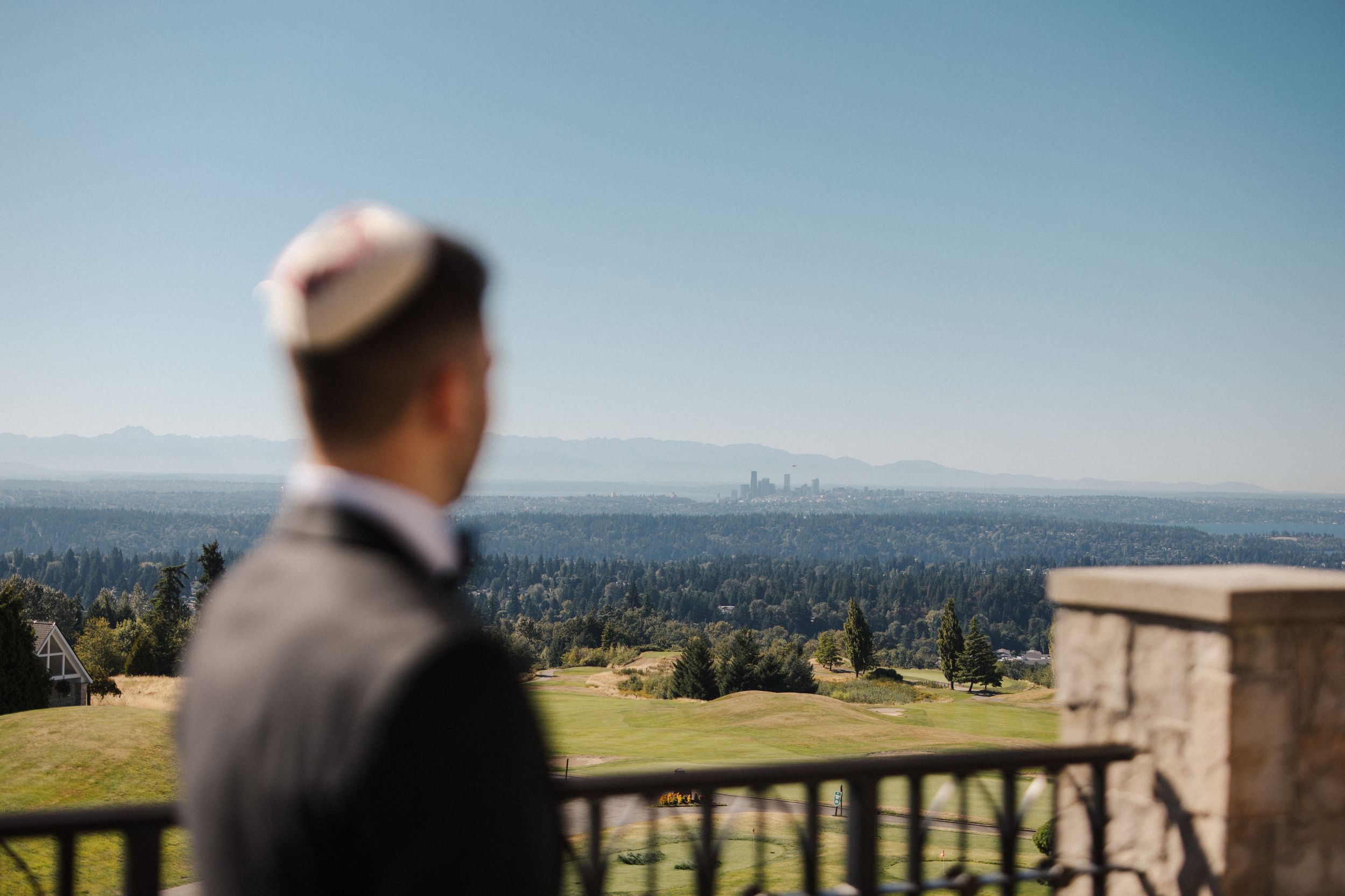 Panoramic cityscape views from a hilltop observation point with stone railing and visitors enjoying the scenery.