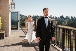 Couple in formal attire walking along an outdoor terrace with scenic mountain views in the background.