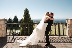 A romantic wedding moment captured on a scenic terrace overlooking a landscape with evergreen trees and blue skies.