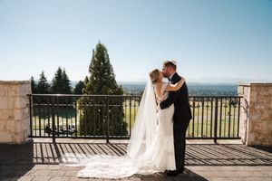 A romantic couple embraces on a stone terrace overlooking a scenic mountain landscape on their wedding day.