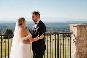 A couple in wedding attire embraces on a scenic balcony overlooking a mountainous landscape.