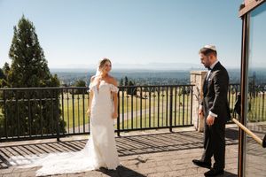 A couple shares their first look moment on a scenic balcony overlooking a mountainous landscape on their wedding day.