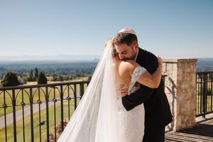 Couple shares romantic moment on stone balcony overlooking scenic mountain landscape during wedding photoshoot.