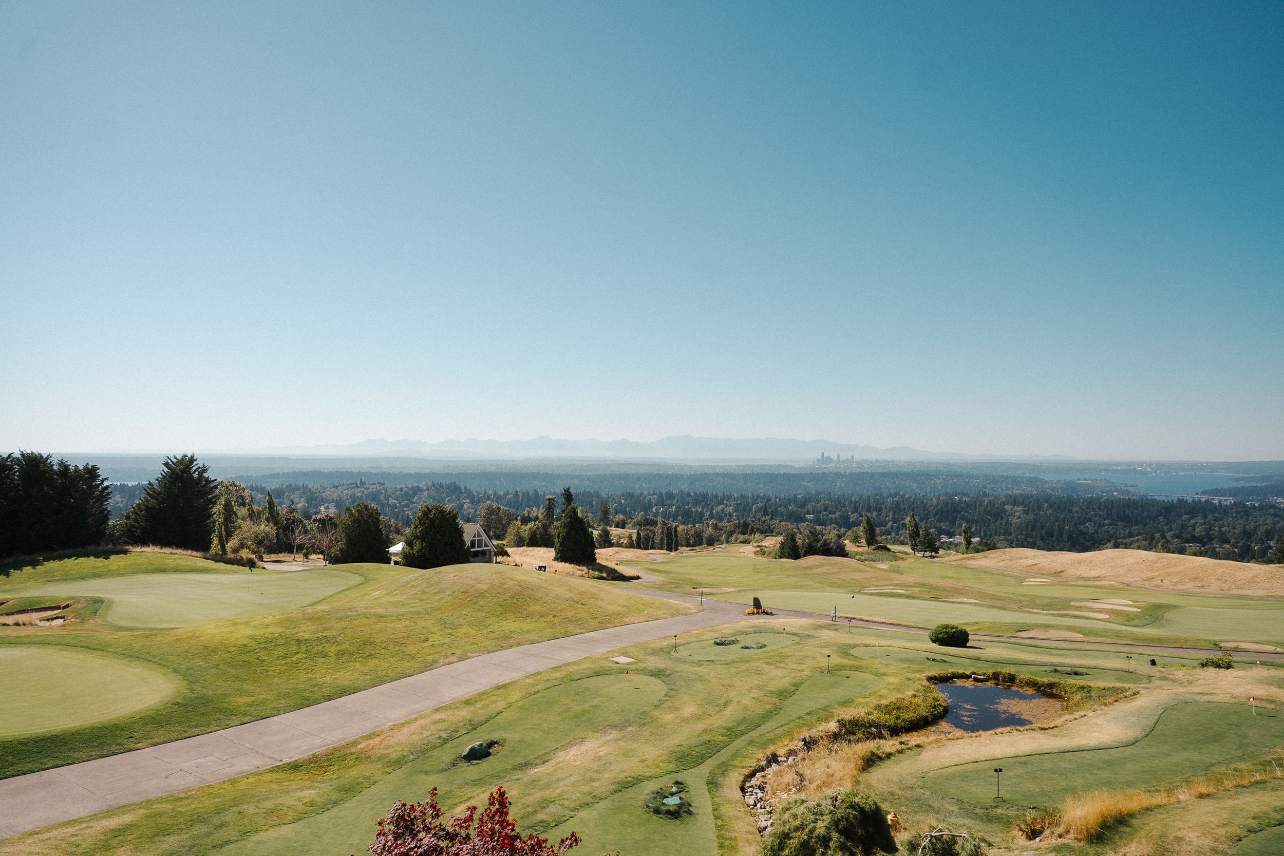 Panoramic view of a golf course with rolling hills, winding paths and lush green fairways stretching into the distance.