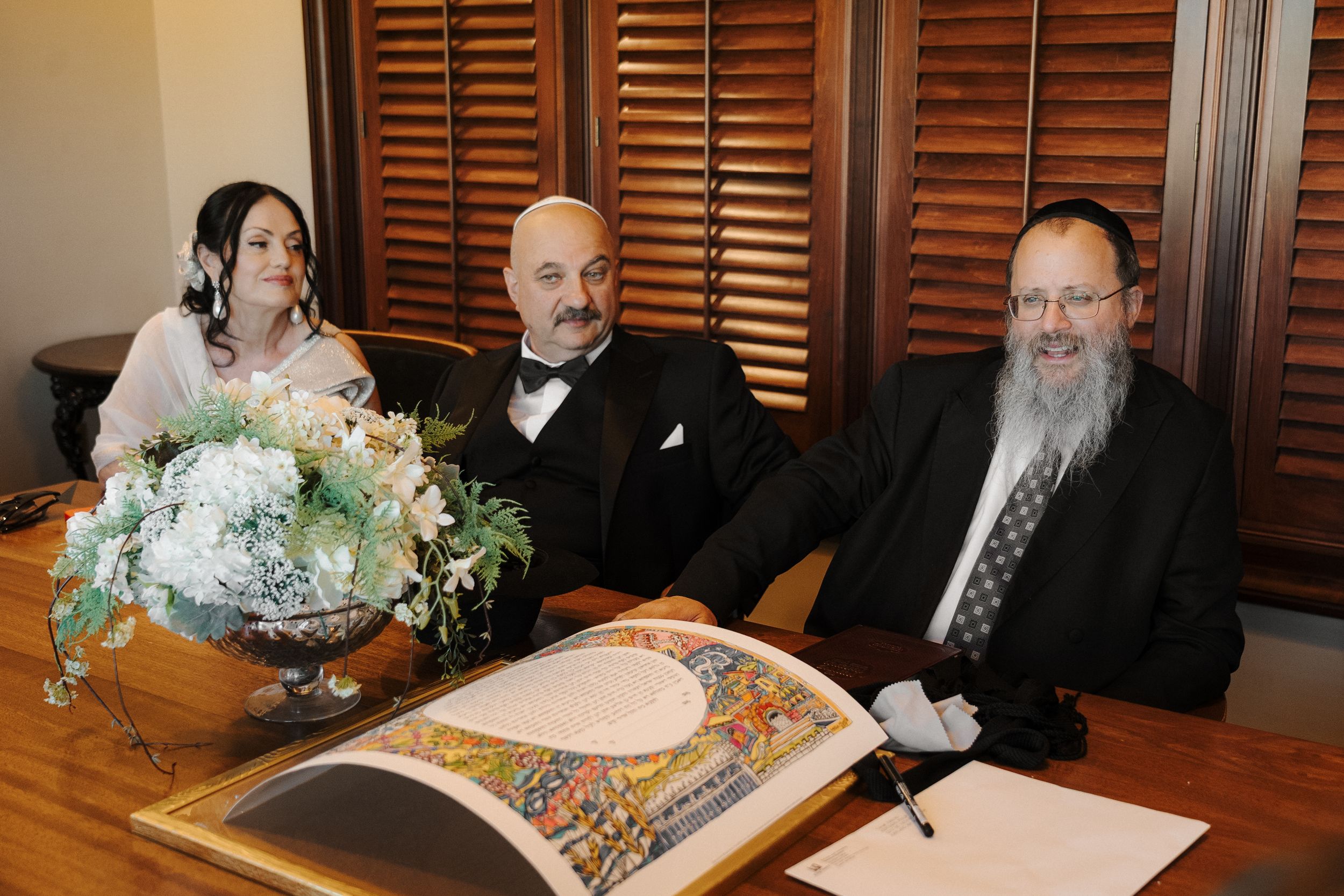 A group sits at a long dining table in a restaurant with wooden shutters and warm lighting in the background.