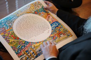 A couple reads from a beautifully illustrated book with colorful illuminated borders and decorative artwork.