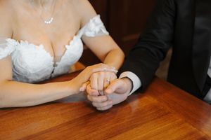 Hands rest on a wooden table during what appears to be a formal occasion with formal attire visible.