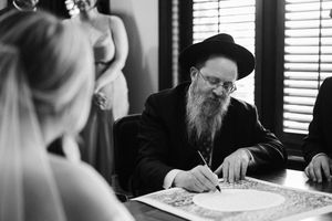 A traditional Jewish wedding ceremony with the rabbi signing the ketubah marriage contract in black and white.