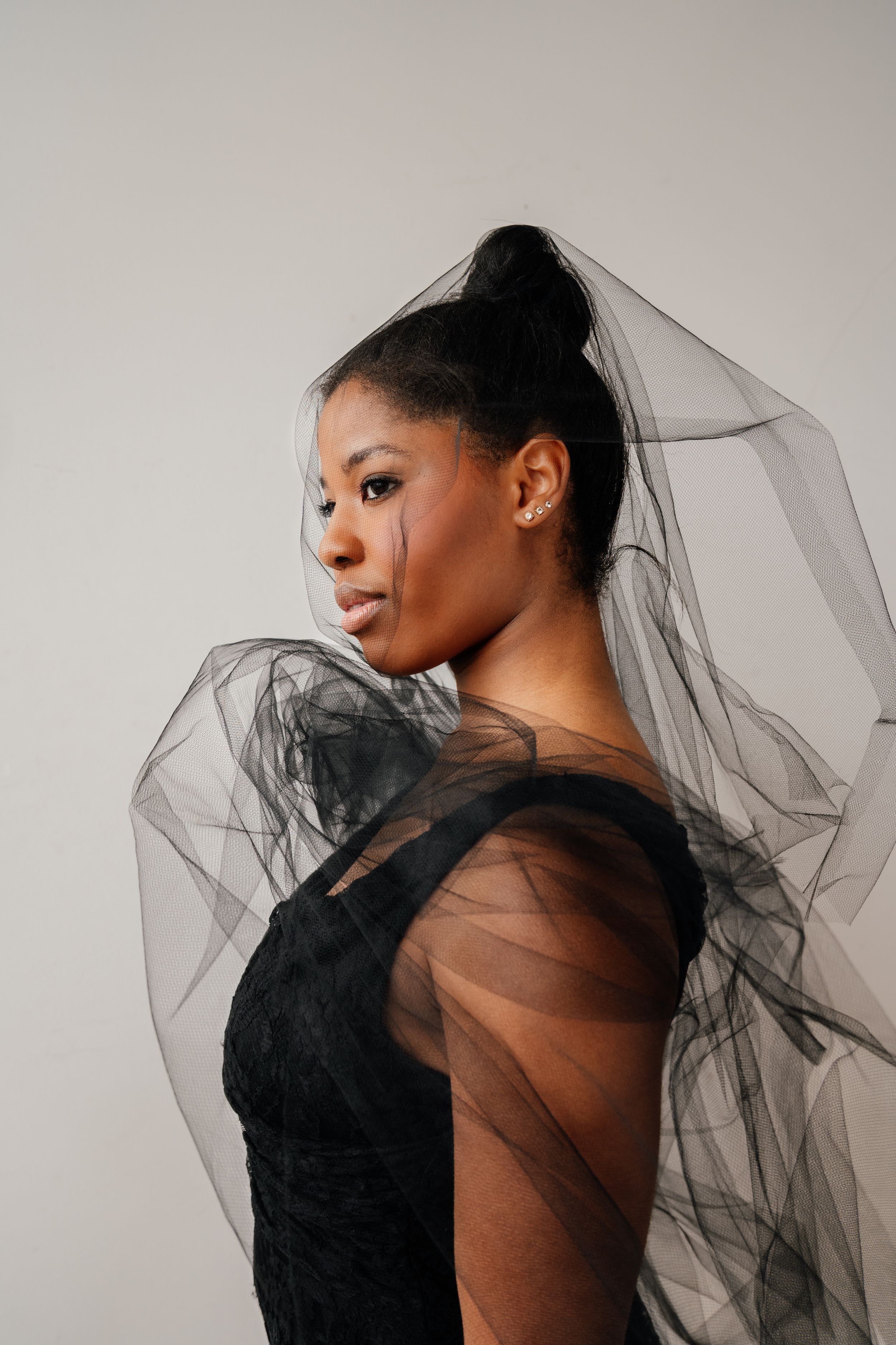 A series of artistic portrait photographs showing a figure draped in sheer black tulle fabric against a light gray background.