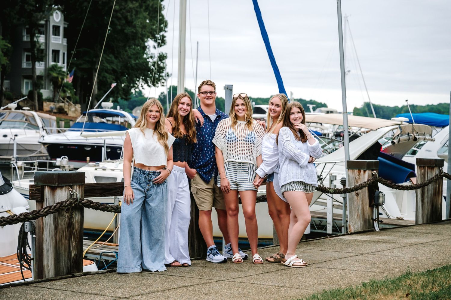 A group of people in light colored clothing gathered at a marina dock during a summer day.