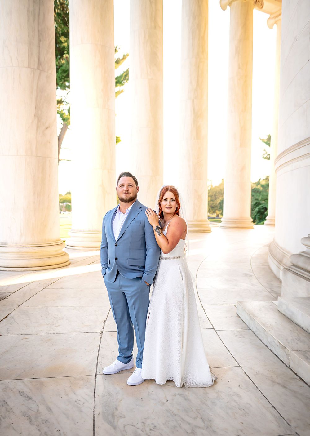 Newlywed couple poses elegantly between white marble columns at a grand architectural venue.