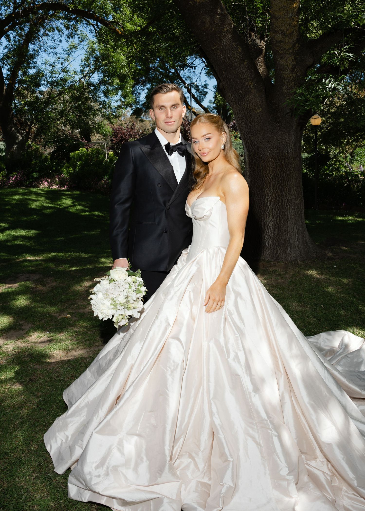 A bride in a white strapless wedding dress smiles while holding a delicate bouquet of white flowers and greenery at Al Ru Farm in Adelaide.