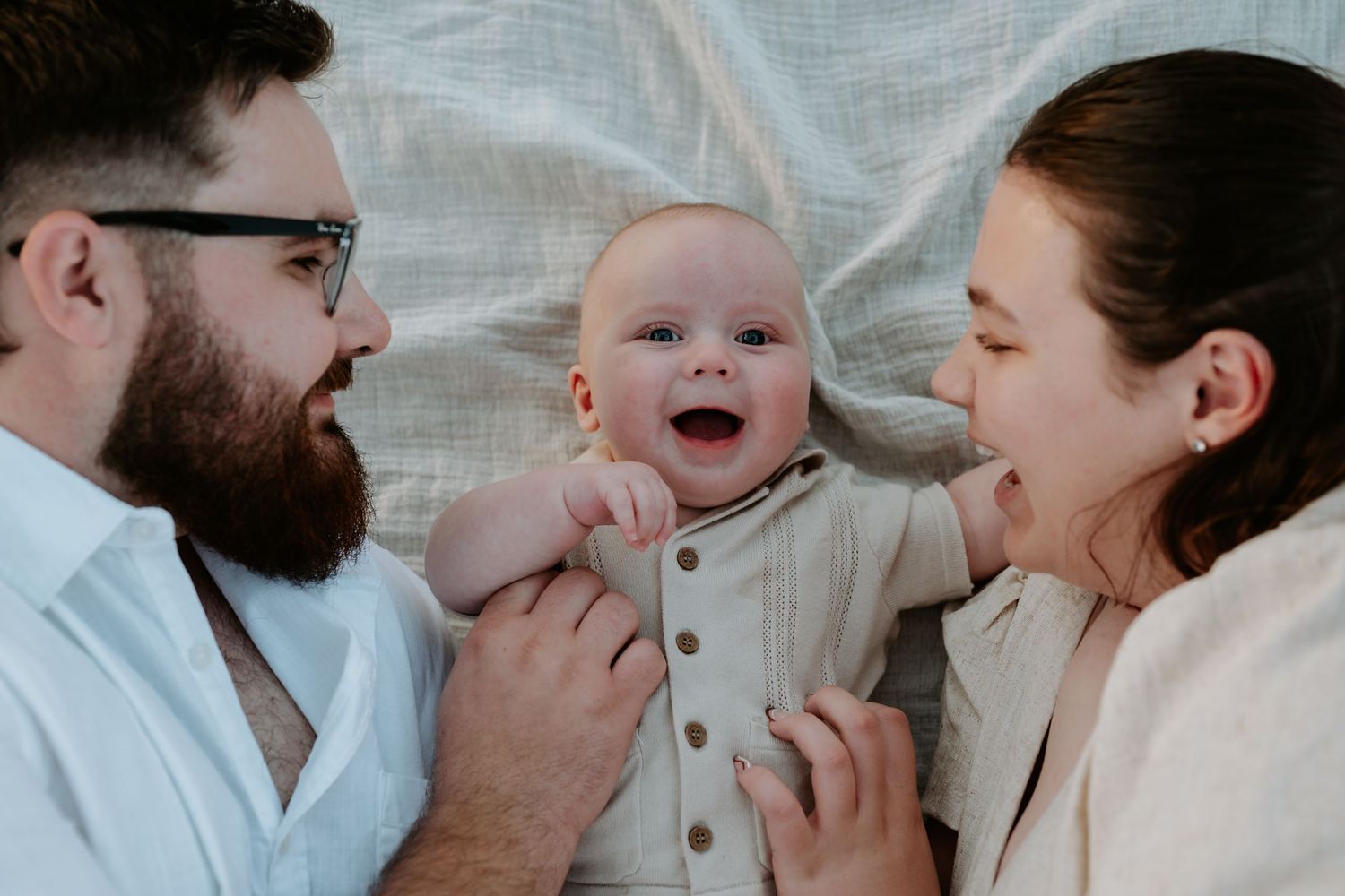 A tender family moment showing parents and baby interacting with joyful expressions on a light background.
