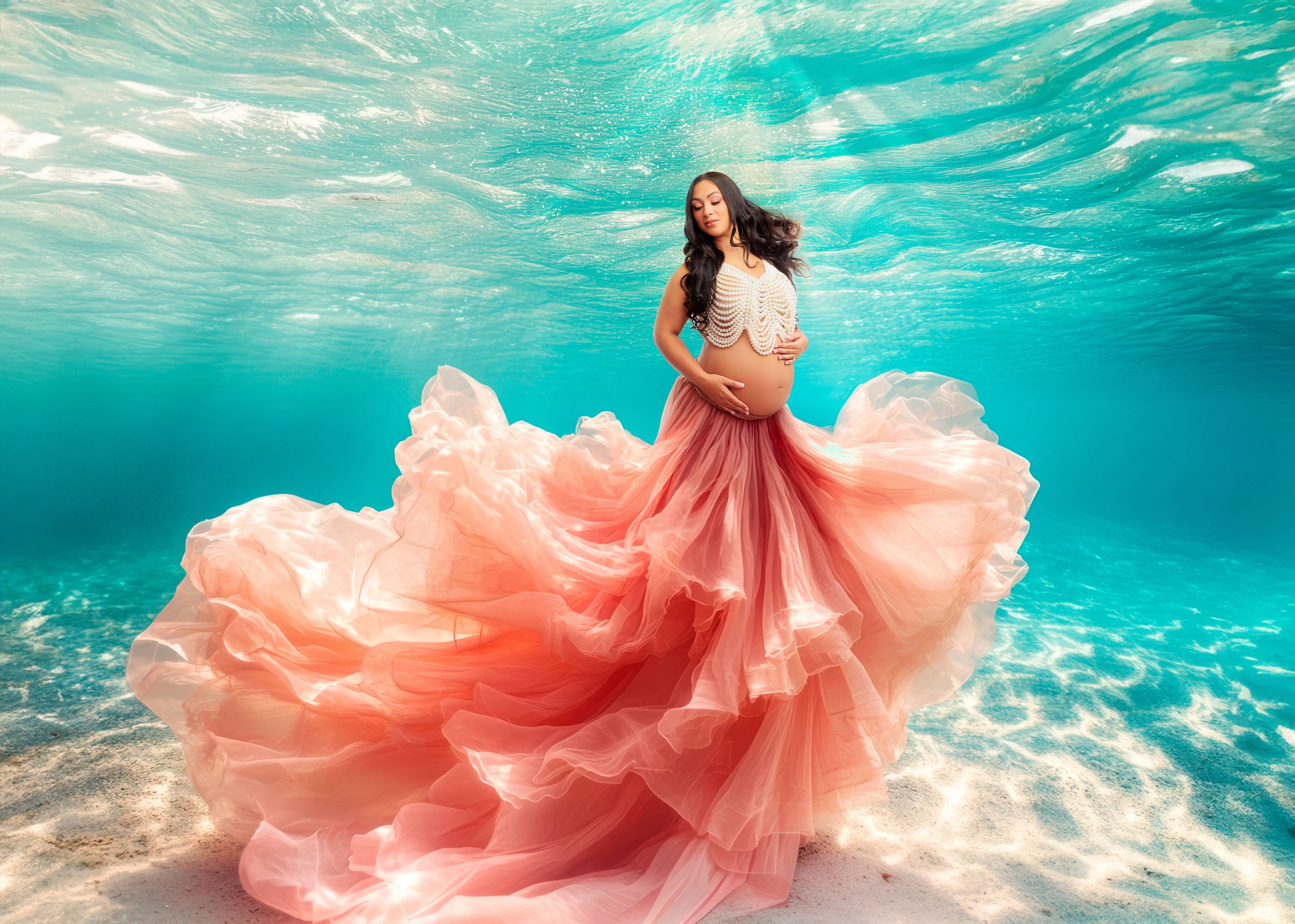 Pregnant woman in flowing pink gown poses gracefully in stunning underwater maternity photo.