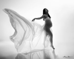 Black and white maternity photo of pregnant woman with flowing white fabric.