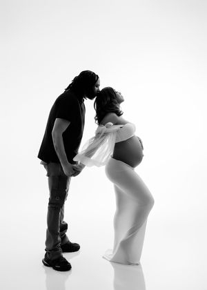 Black and white maternity photo of couple sharing tender kiss in minimalist studio.