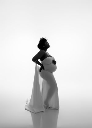 Elegant black and white silhouette of pregnant woman in white gown against bright backdrop.