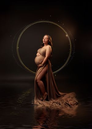 Pregnant woman wrapped in golden fabric stands in water before glowing gold circle on dark background.
