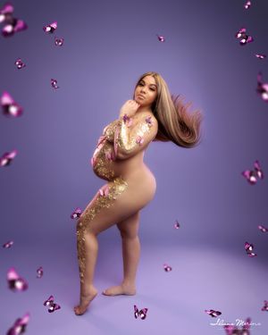 Pregnant woman with gold glitter body art poses with butterflies on purple studio background.