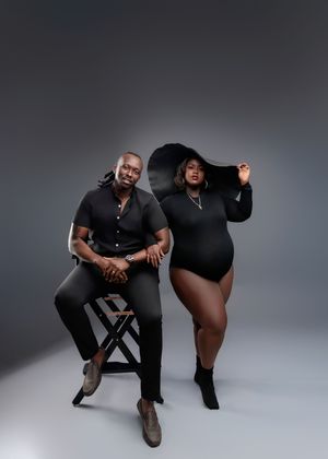 Expecting couple in matching black outfits pose together in a stylish studio maternity photography session.