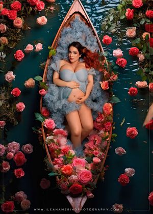 Aerial view of pregnant woman in blue ruffled outfit lying in boat surrounded by roses.