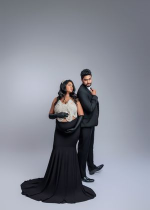 Elegant pregnant couple in black formal wear pose back-to-back in stylish maternity shoot.