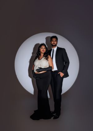 Couple in black formal attire pose before circular spotlight in dramatic maternity portrait.