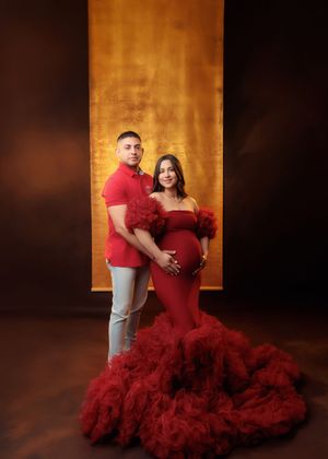 Couple in matching red outfits pose together in elegant maternity photography session.