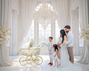 Elegant family maternity photo shoot in white studio with chandelier, gold pram, and flowing drapes.