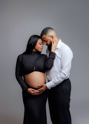 Intimate couples maternity portrait in black and white outfits against gray studio background.