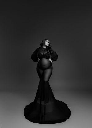 Black and white maternity portrait of pregnant woman in elegant black mermaid gown in studio.