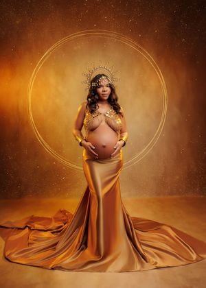 Pregnant woman wearing gold crown and satin skirt poses within glowing golden circle on warm background.
