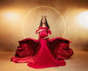 Pregnant woman in flowing red gown with gold crown poses regally in stunning maternity portrait.