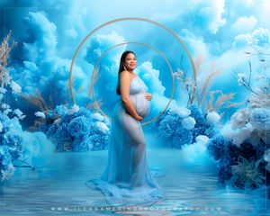 Pregnant woman in sheer blue gown poses among blue flowers and clouds in dreamy maternity portrait.