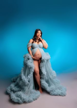 Pregnant woman in blue ruffled tulle gown posing against vibrant blue backdrop.