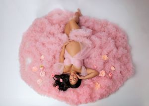 Pregnant woman lying on pink tulle gown surrounded by roses, aerial view.