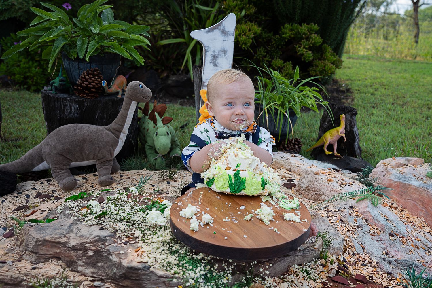Little boy eating cake during a professional outdoor dinosaur cake smash photo shoot.