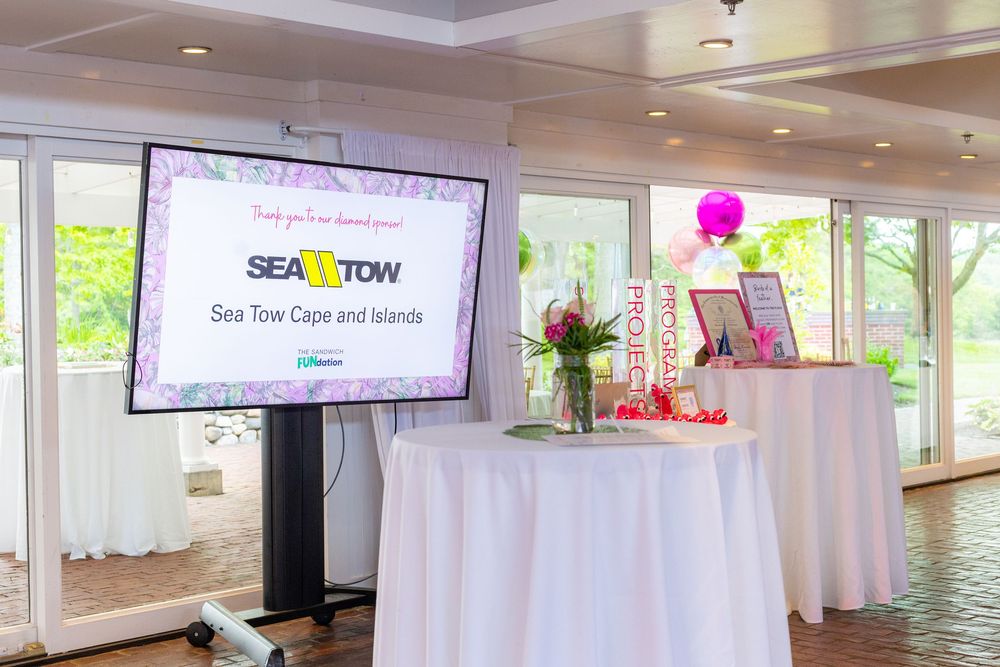 Modern event venue interior with white walls, hardwood floors, mounted TV screens and pink balloon decorations.
