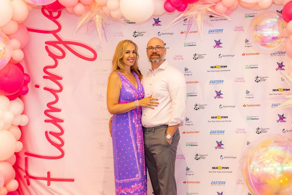 People pose for photos at a red carpet event with pink lighting and branded step-and-repeat backdrop.