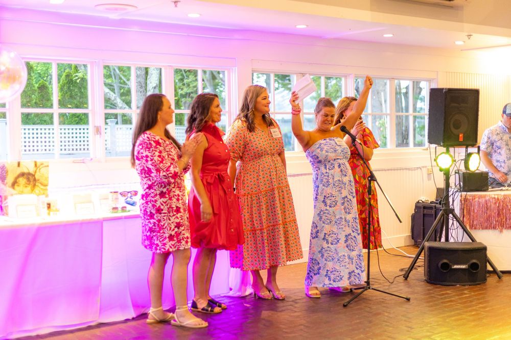 A group of women in colorful floral dresses perform together on stage with purple lighting at an event.