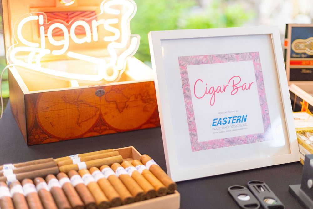Colorful display of cigars and tobacco products arranged in a retail store showcase with framed signs and price tags.