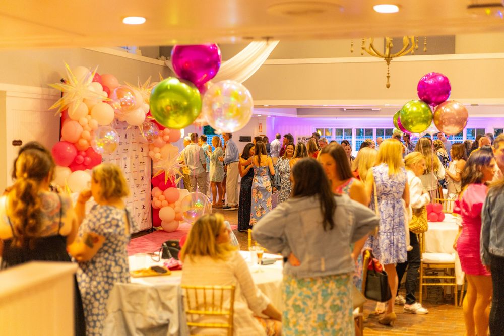 A festive party venue decorated with colorful balloon arrangements and filled with guests mingling at tables.