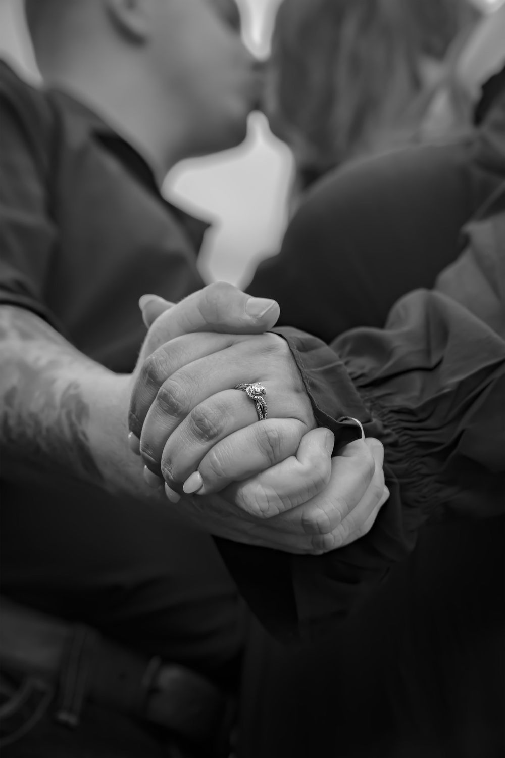 Close up black and white photo of clasped hands showing an engagement ring.